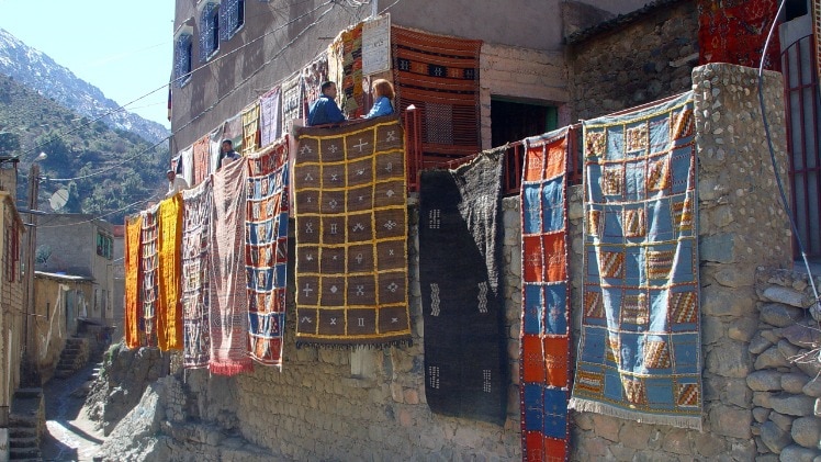 A couple of real-world carpets hanging on a building, with a mountain in the background.